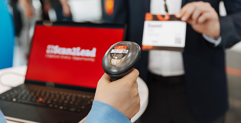 Mitarbeiter scannt mit dem STATION-Handscanner den Badge eines Besuchers am Laptop – Leads direkt während des Gesprächs qualifizieren.