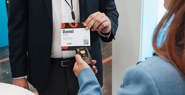 Nahaufnahme: Eine Mitarbeiterin scannt mit dem COLLECT-Miniscanner den QR-Code auf dem Badge eines Besuchers – Lead-Erfassung in Sekunden.