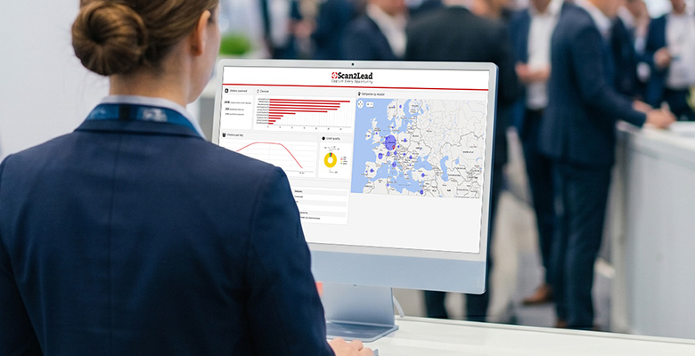 Standmitarbeiterin betrachtet am Monitor das Scan2Lead PORTAL mit Diagramm und Karte – erfasste Leads werden nahtlos ins PORTAL übertragen.