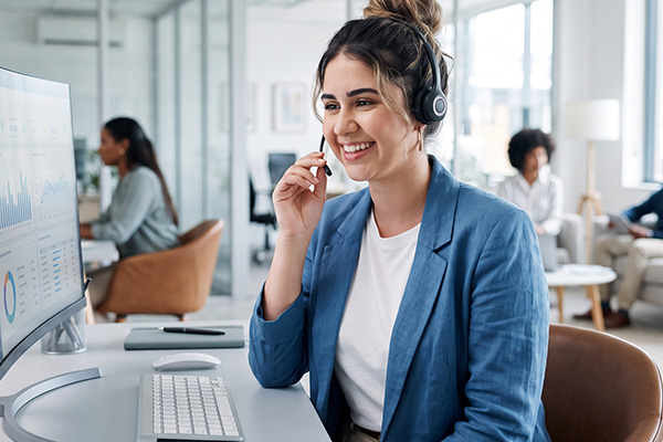 Lächelnde Support-Mitarbeiterin mit Headset am Bildschirm in einem hellen Büro.