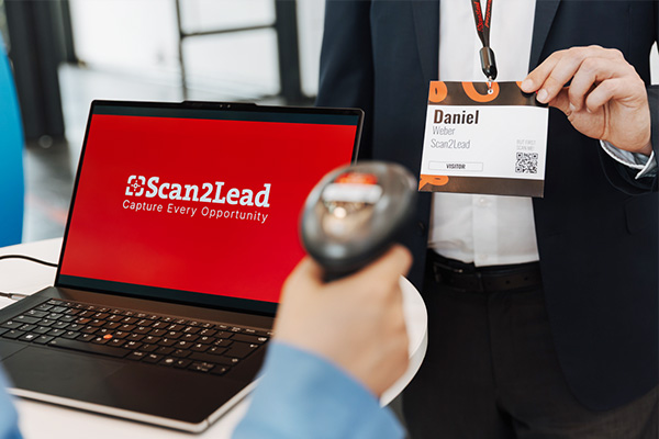 Mitarbeiter scannt mit dem Handscanner den Badge eines Besuchers am Laptop mit Scan2Lead-Oberfläche – Badge-Scan am Counter.