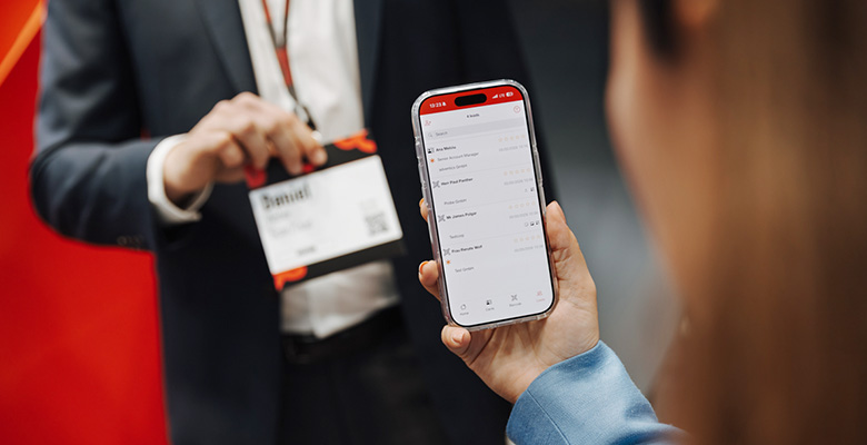 Person hält ein Smartphone mit geöffneter Scan2Lead App und der Lead-Liste am Messestand.